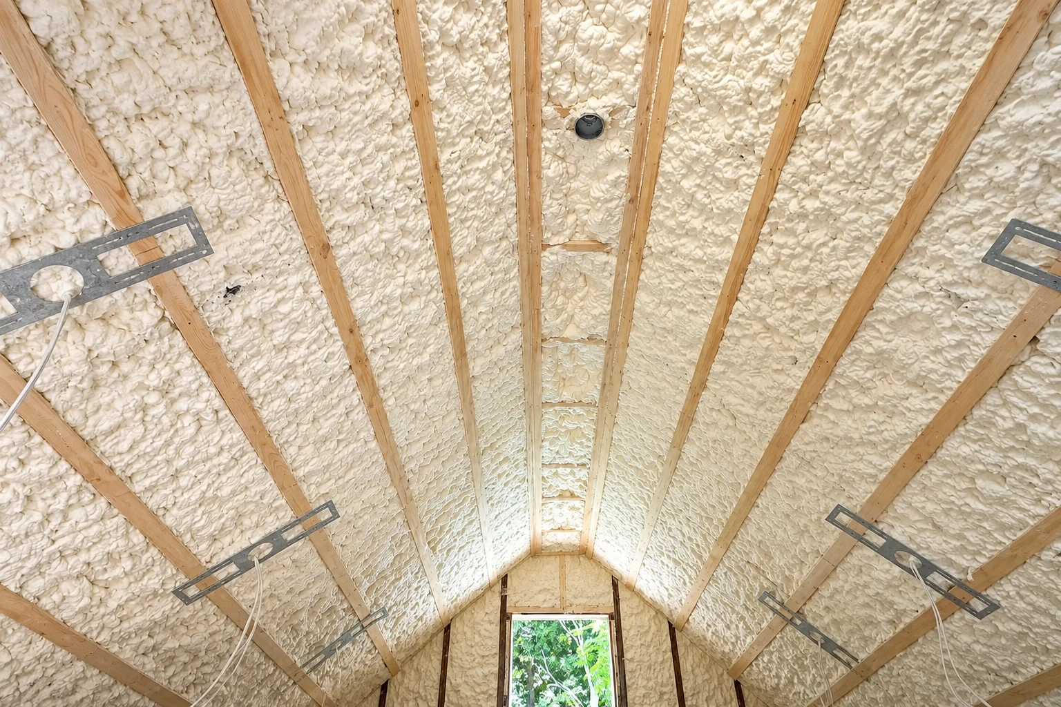 Vaulted ceiling and walls coated in white spray foam between exposed wooden rafters.